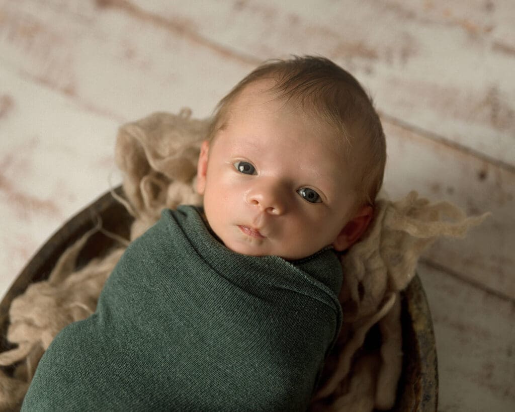 Newborn boy wide awake wrapped in a dark green wrap.