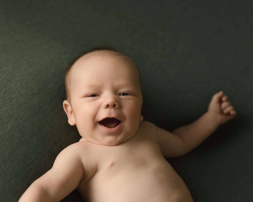 Newborn boy laying on green fabric smiling.