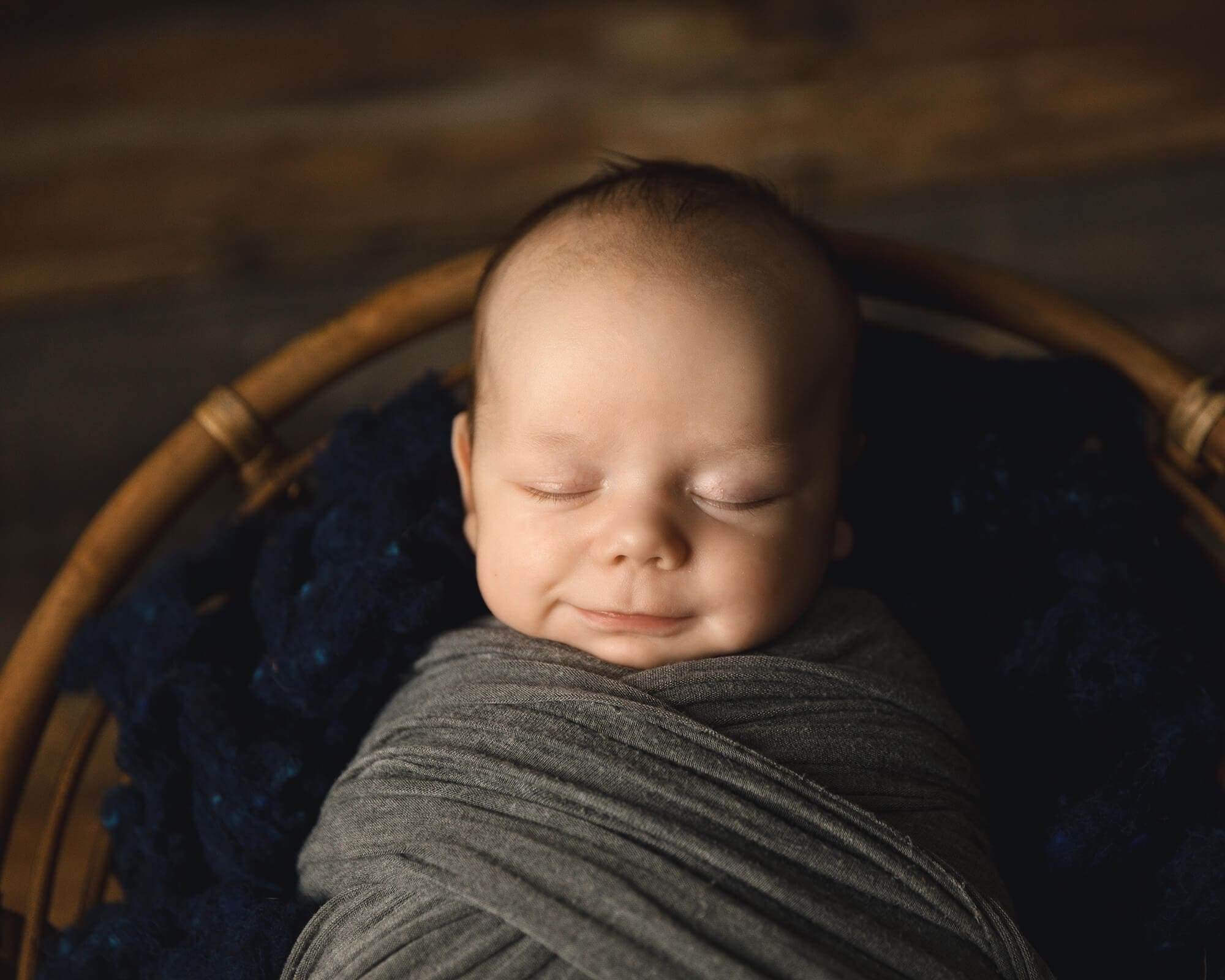 Newborn boy wrapped in a gray wrap sleeping peacefully.