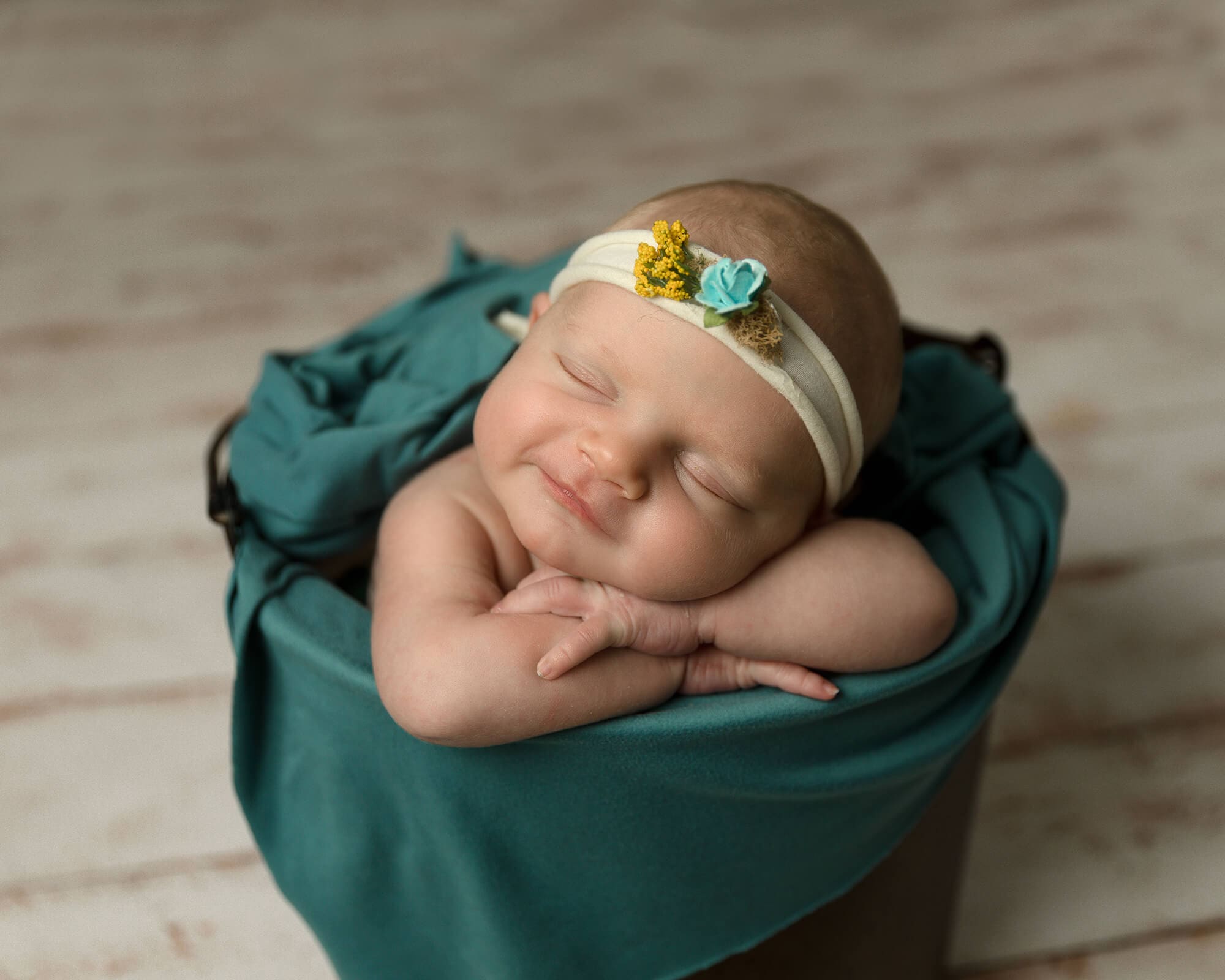 Newborn girl in a bucket sleeping on her arms.