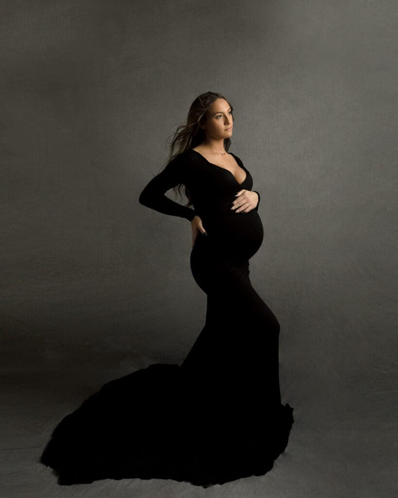 Pregnant woman dressed in a black maternity gown and gray background.