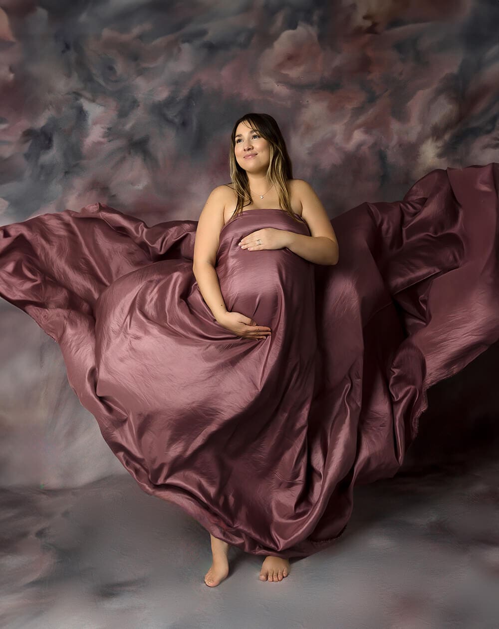 Pregnant woman with mauve satin silk flowing around her.